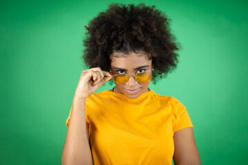 African american woman wearing sunglasses and orange casual shirt over green background with a happy face standing and smiling with a confident smile showing teeth