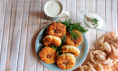 Homemade fried dough with minced meat or belyashi. Pies are on a plate on a white wooden table. Top view. Copy space.