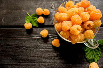 Ripe yellow raspberry with green leaves in a glass Cup on a wooden background. The concept of healthy eating. Vegan, Keto, Paleo diet. Top view. Copy space