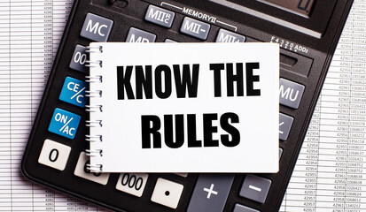 On the table are reports, a calculator and a card with the words KNOW THE RULES on it. Business concept