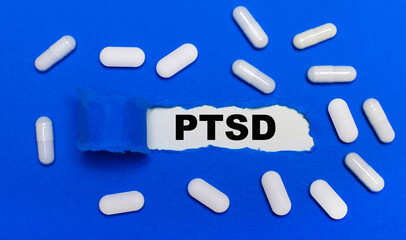 White pills lie on a beautiful blue background. In the center is white paper with the inscription PTSD. Medical concept. View from above.