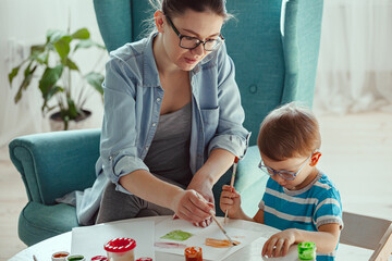 Mother or art therapist and child paint watercolor together at home