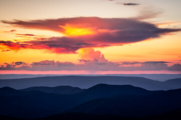 A anvil shaped cloud which is producing a small shaft of rain catches fire in the sunset light over the Blue Ridge Mountains.