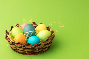 Easter set of colorful eggs in a wicker basket on a green paper background.