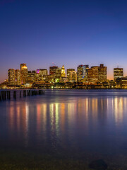 Boston Nightscape Skyline and Weathered Pier with Damaged Pilings. Harmony of Nature, Civilization, and Reflections of Lights and Time.