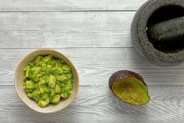 Fresh chunky guacamole in bowl and empty avocado skin halves on bright background. Top view.