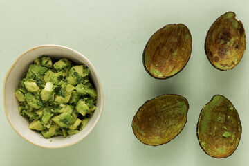 Fresh chunky guacamole in bowl and empty avocado skin halves on bright background. Top view.