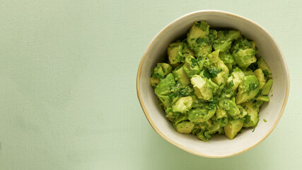 Bowl of freshly made chunky guacamole on bright green background with copy space for text, top view.