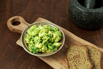 Avocado guacamole in bowl and slices of homemade bread on table. Vegan cuisine.