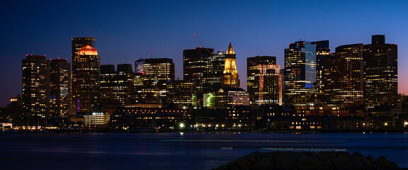 Panoramic Night Cityscape Boston Skyline over Boston Harbor. Dark Twilight Modern City Photo with Water Reflections.