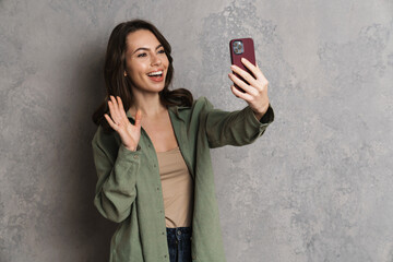 Fototapeta premium Happy nice girl waving hand while taking selfie on mobile phone