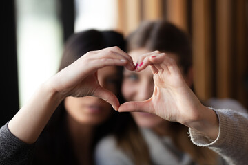 Two lovely girls smiling in a cafe and making a hearth shape with their hands.