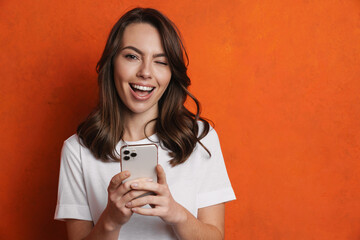 Cheerful charming girl winking and using mobile phone