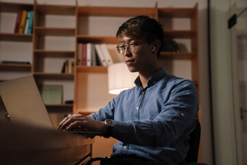 Fototapeta premium Focused asian guy working with laptop while sitting at table in office