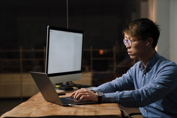 Focused asian guy in earphones working with laptop and computer