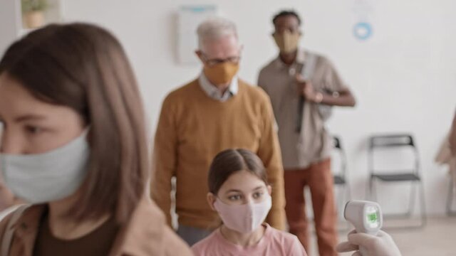 Medium Steadicam Of Diverse Hospital Patients Wearing Protective Face Masks, Moving In Line, Getting Their Body Temperature Checked With Contactless Infrared Thermometer