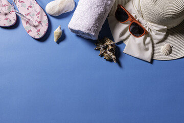 Top view of sunglasses, a straw hat, sandals, a towel and sea shells on a blue background