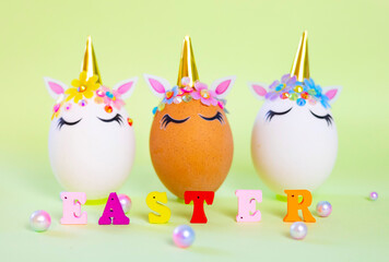 brown and white Easter eggs decorated in the form of unicorns and wooden letters Easter on a green and yellow background, a minimal creative concept of a happy Easter