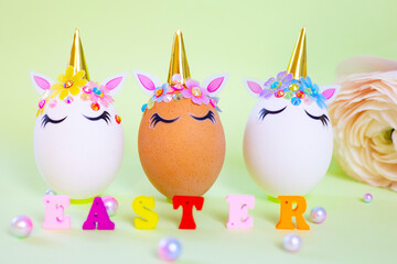 brown and white Easter eggs decorated in the form of unicorns and wooden letters Easter on a green and yellow background, a minimal creative concept of a happy Easter