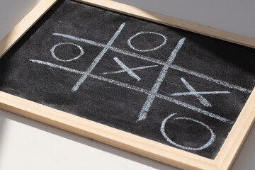 The tic tac toe game on blackboard with chalk grid, naughts and crosses