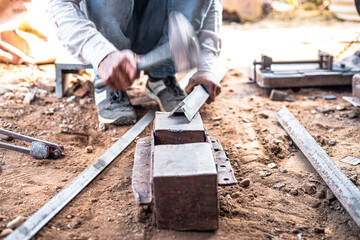 Closeup hands of a blacksmith hits iron or steel sheet with a hammer at a workshop outdoors.