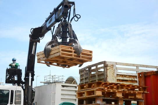 Workers are controlling machine loader manipulator with hydraulic multi valve crab bucket or crane garbage truck uploads industry waste this is pallets wood to transport for recycle.