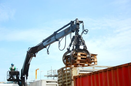 Workers are controlling machine loader manipulator with hydraulic multi valve crab bucket or crane garbage truck uploads industry waste this is pallets wood to transport for recycle.