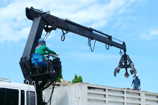 Workers are controlling machine loader manipulator with hydraulic multi valve crab bucket or crane garbage truck uploads industry waste this is pallets wood to transport for recycle.