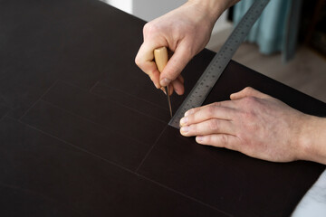 Men's hand holding a awl and metal ruler and working on a leather wallet in his workshop. Working...