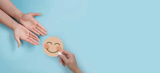 Hand holding nude paper cut happy smile face give it to another person on blue background, positive...