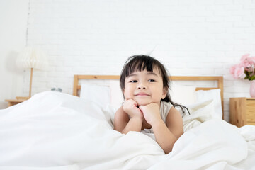 An asian toddler girl 3 years old lie on her stomach in bed and rest her chin on hands