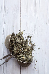 Dry raspberry leaves in a tea strainer close-up. Alternative herbal medicine. Healthy lifestyle concept. Composition with organic, natural herbal tea on a light wooden table.
