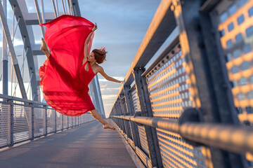 Beautiful redhead female dancer in long red skirt freezed in motion while gracefully jump in the...