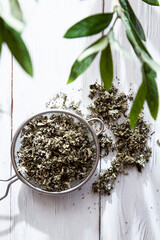 Dry raspberry leaves in a tea strainer close-up. Alternative herbal medicine. Healthy lifestyle concept. Composition with organic, natural herbal tea on a light wooden table.