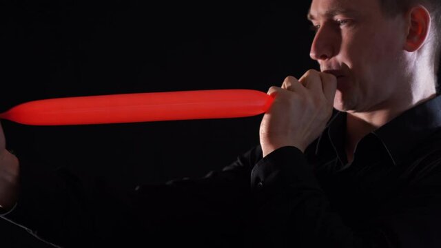 Man inflating long balloon by his length isolated on black background 