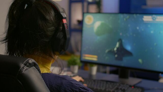 Cyber gamer playing space shooter video game using RGB keyboard and professional headset during gaming tournament. Player talking with multiple players using headphones while streaming video games