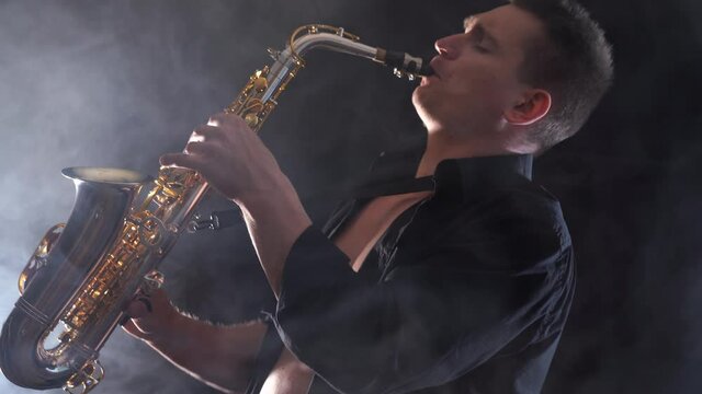 man wearing black shirt playing on saxophone isolated on smoked background 