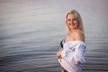 blonde girl in a white man's shirt on the riverbank, selective focus