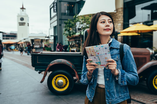 asian girl studying abroad holding map is looking at the surroundings by pickup truck. female exchange student looking forward to exploring new places and trying new things. authentic lifestyle - Powered by Adobe