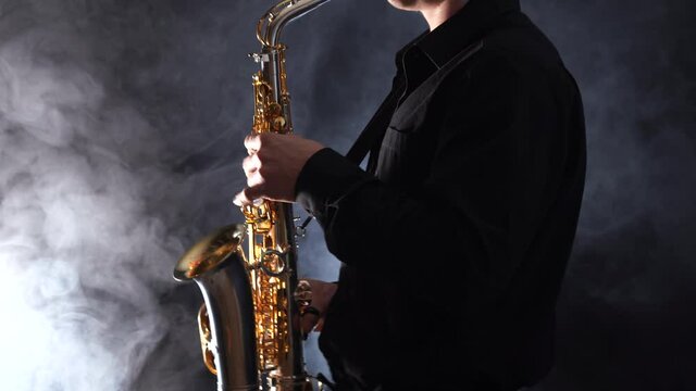 Closeup of hands playing on saxophone isolated on smoked background 