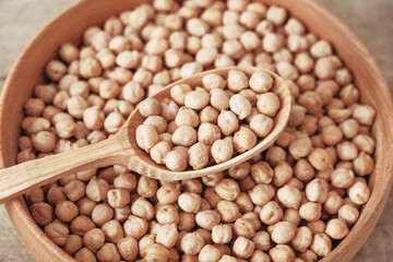 Raw chickpeas in a wooden plate and spoon on an rustic wooden background. Top view. Copy, empty space for text