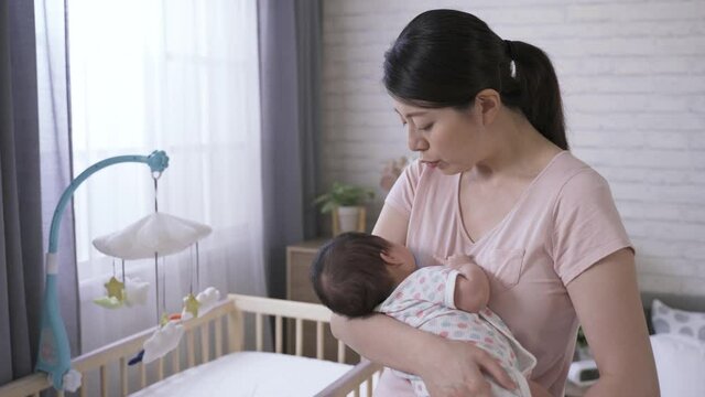 beautiful Taiwanese mom is looking at her baby daughter affectionately while putting her to sleep with verbal soothing and gentle pat in the bedroom.