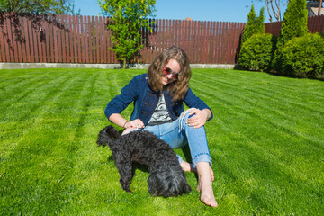 Junges Mädchen mit Retro Sonnenbrille spielt mit  ihrem schwarzen Bichon Hund