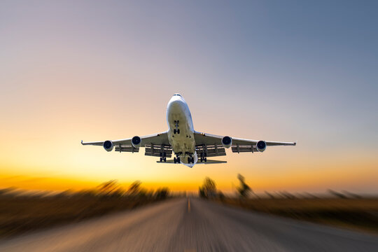 front image commercial passenger aircraft or cargo transportation airplane fly up taking off from airport runway motion blur effect in morning with sunrises landscape view