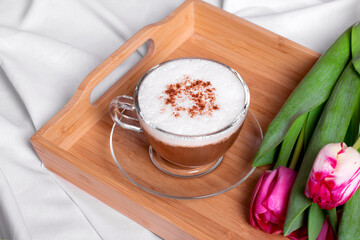 Coffee with cinnamon and pink tulips on the wooden tray in bed. Romantic surprise