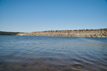 Obraz premium Scenic view over wide river and it's bank. Beautiful natural countryside landscape with blue sunny sky. Summer getaway vacation into isolated places. Calm water - perfect for meditation.