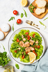 Salad with baked salmon fish. Green salad mix with tomatoes and salmon. Top view at white table.