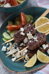 Close-up of bbq meat kofta with feta cheese and vegetables served on a turquoise plate, vertical shot