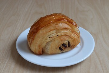 Chocolate croissant on a white plate on a wooden table background