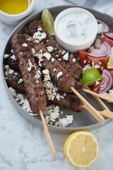 Closeup of roasted greek kofta kebabs with served with feta cheese and tzatziki sauce, vertical shot on a grey marble surface